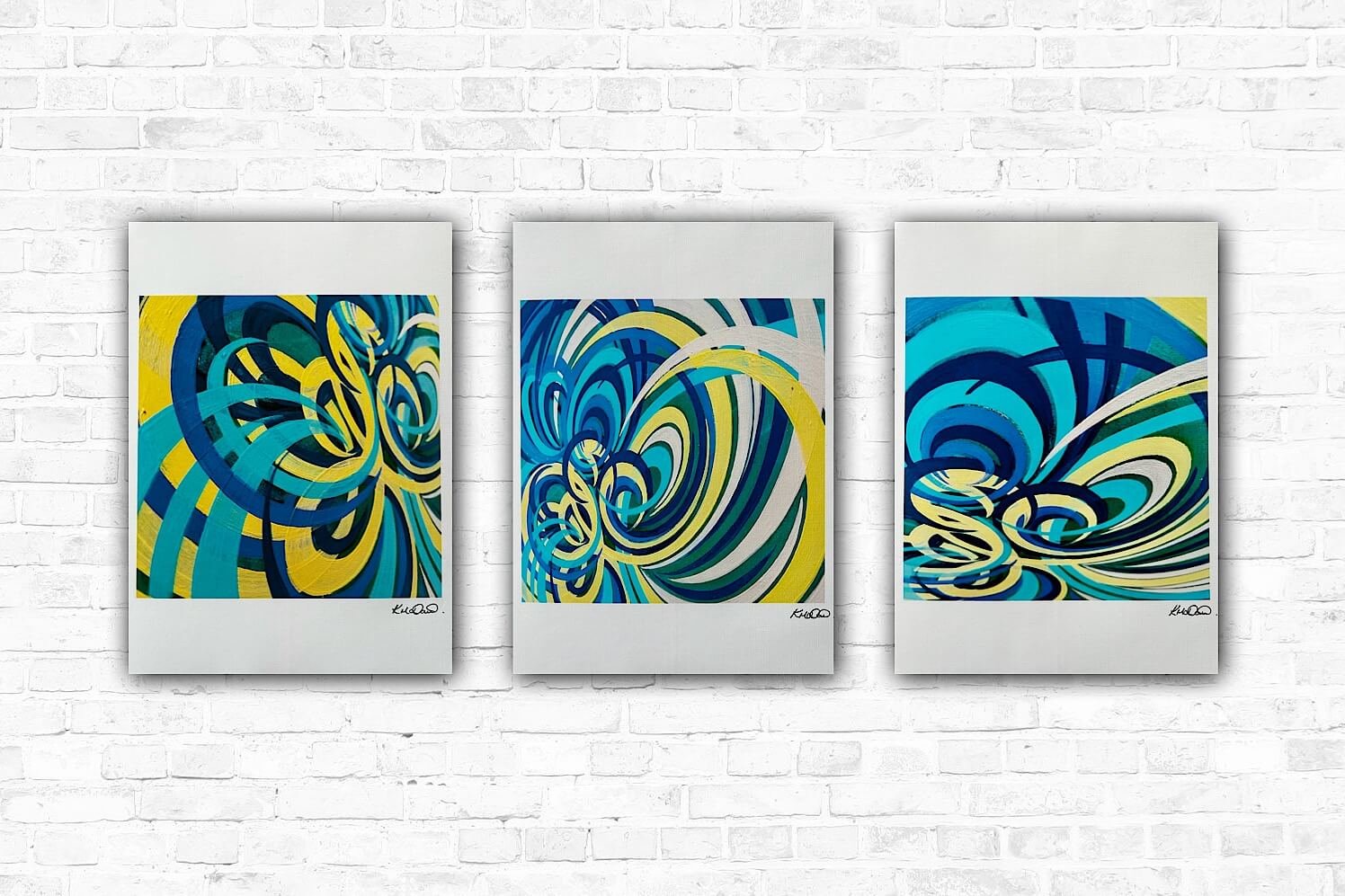 A set of three colourful prints displayed side by side against a white brick wall background.