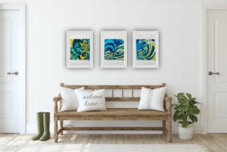 Wooden bench with white pillows in a room with a trio of framed abstract art prints on the wall.
