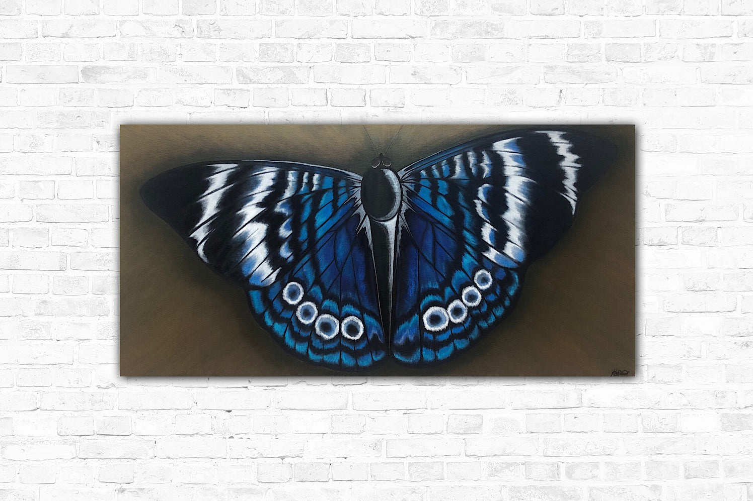A butterfly wall art decor of a vibrant butterfly with blue, black, silver, and white colours, displayed against a brick wall background.