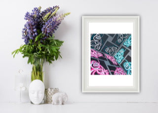 Framed abstract paper art, framed on a white wall with a vase of flowers and decorative items.