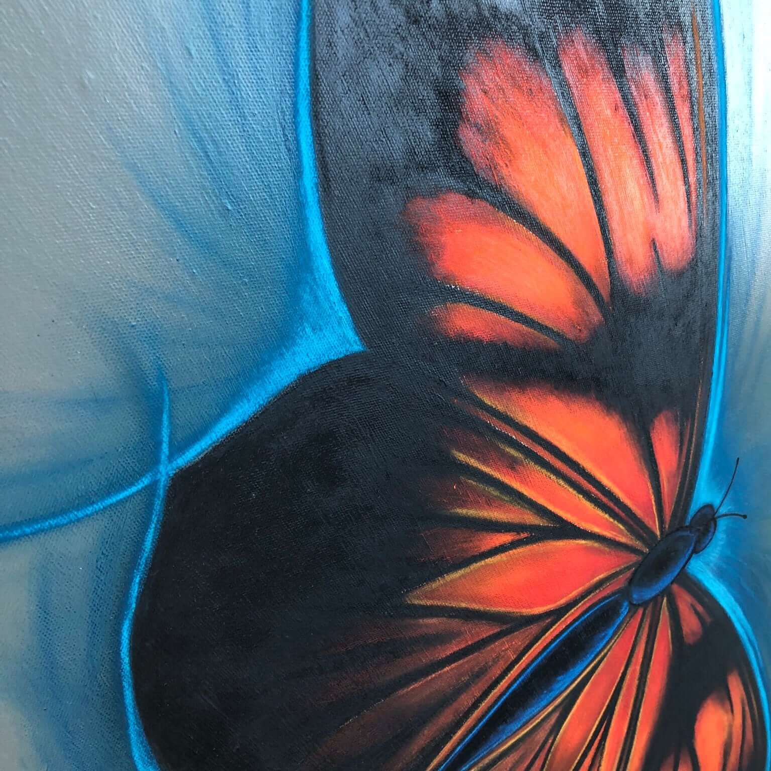 Close-up of a hand-painted butterfly painting with vibrant orange and black wings against a blue background, highlighted with soft chalk pastels.