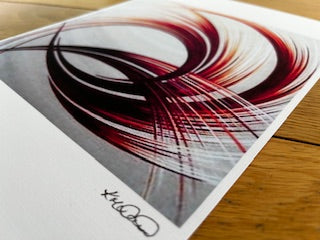 Abstract colourful pattern on a piece of paper with a signature at the bottom, placed on a wooden surface.